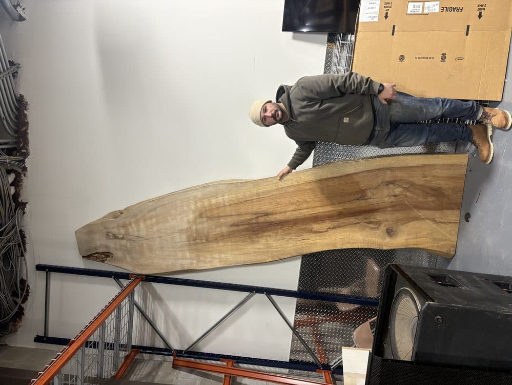 Michael Palmer holding a large live edge wood slab in the Coastal Custom Woodworks workshop