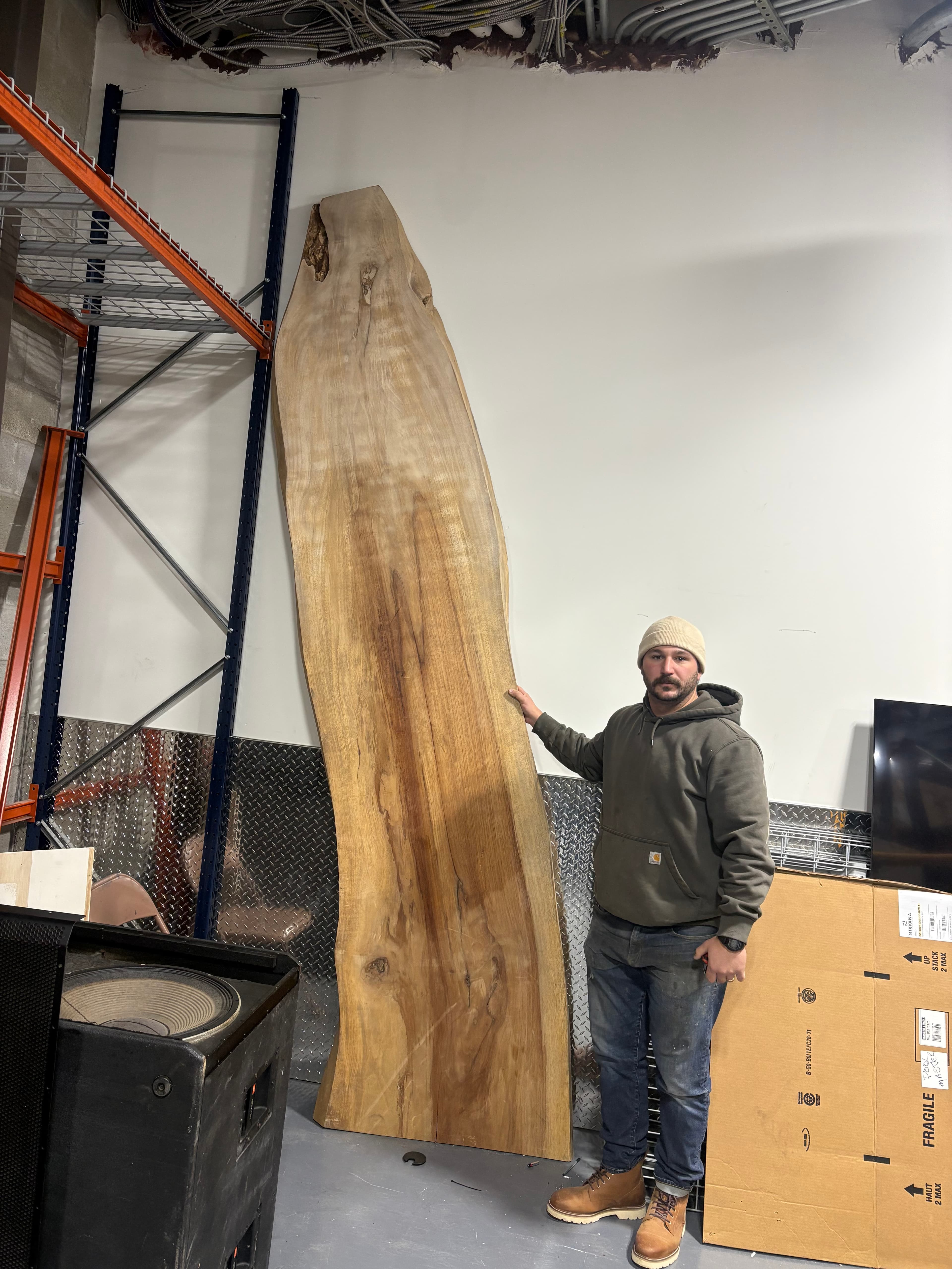 Michael Palmer holding a large live edge wood slab in the Coastal Custom Woodworks workshop