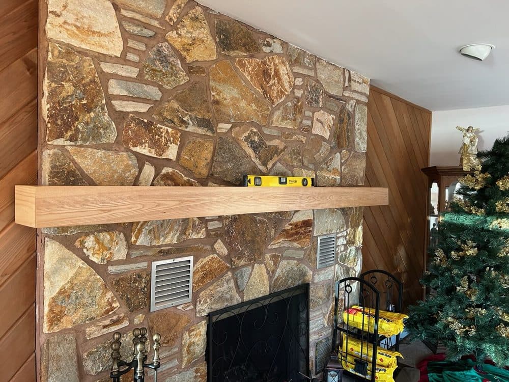 Custom oak fireplace mantel installed on a stone accent wall