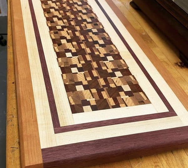 End-grain cutting board with chaotic pattern bordered by purpleheart and maple