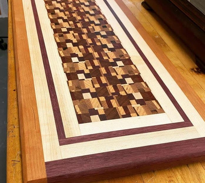End-grain cutting board with chaotic pattern bordered by purpleheart and maple