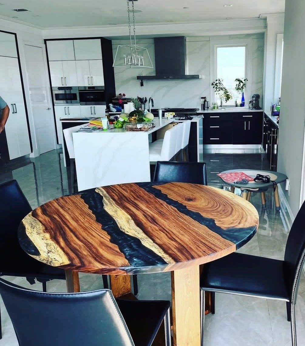 Round epoxy resin dining table with warm monkeypod wood and dark navy resin rivers in modern kitchen